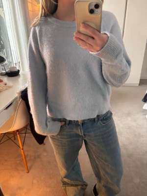 Ljusblå stickad tröja - Mysig ljusblå stickad tröja med rund hals och långa ärmar. Tröjan har en avslappnad passform och ribbade muddar vid ärmslut och nederkant. Perfekt att bära till jeans för en enkel och stilren look. I alpacka och ullblandning