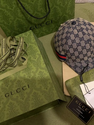 Gucci GG Supreme keps blå/beige - Säljer en snygg Gucci keps i GG Supreme-mönster i blått och beige. Kepsen har klassisk böjd skärm, justerbar rem bak och röda/blå ränder på sidan. Materialet är canvas med läderdetaljer och kepsen har tydlig logga över hela ytan. Perfekt för dig som gillar lyxig streetstyle.