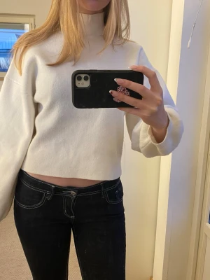 Vit stickad tröja - Säljer en vit stickad tröja med hög hals och långa ärmar. Tröjan har en enkel och stilren design med mjukt material och ribbade muddar vid ärmsluten. Perfekt för en trendig och avslappnad look.