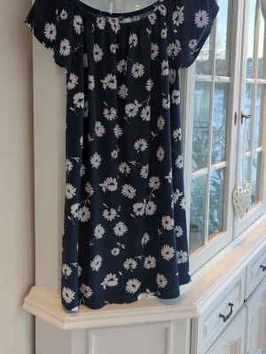 Marinblå blommig kortklänning - Söt marinblå kortklänning från 157 med vitt blommönster. Klänningen har offshoulder-modell med resår upptill och ett ledigt, flowy fall. Perfekt för dig som gillar en avslappnad och somrig stil.