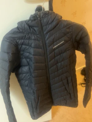 Svart dunjacka från Peak Performance i storlek 34 - Snygg svart dunjacka från Peak Performance med luva och dragkedja framtill. Perfekt för kalla vinterdagar och enkel att matcha till olika outfits. Knappt använd! storlek xs/s