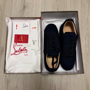 Mörkblå sneakers från Christian Louboutin - Snygga mörkblå sneakers från Christian Louboutin i mocka med klassisk röd sula och guldfärgad logga på innersulan. Skorna har rund tå, svarta snören och diskreta detaljer. Perfekta för dig som vill ha något exklusivt och stilrent. Box med mera medföljer givetvis!