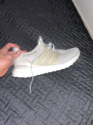 Adidas Ultra Boost vita sneakers - Snygga Adidas Ultra Boost sneakers i vitt med stickad ovandel och vita snören. Skon har en vit Boost-sula och genomskinliga plastdetaljer på sidorna. Perfekta för dig som gillar stilrena och bekväma sneakers med modern design. Har ingen box då jag fick de på födelsedagspresent och vill sälja dom pga storleken va för liten