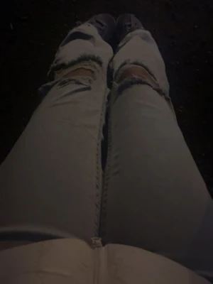 Ljusblå ripped jeans med hål - Säljer ett par ljusblå jeans med stora slitningar och hål över knäna. Jeansen har en rak passform och synliga sömmar framtill. Perfekta för en avslappnad och trendig look.