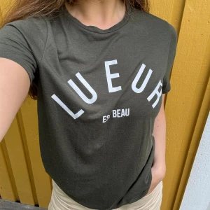 T-shirt med tryck - Mörkgrön (färgen beskrivs bäst på första bilden), skön t-shirt med vitt tryck från River Island. Storlek: (UK) 12. Material: 51% polyester + 49% viskos. Lite lätt nopprig, som ej försvinner med ”nopp-maskin”, men det är knappt synligt. :)