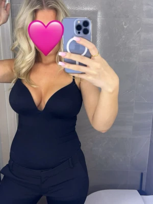 Svart shaping-body med tunna band - Säljer en svart shaping-body med tunna axelband och djup urringning. Bodyn har en slät, figurnära passform och är tillverkad i stretchigt material som formar kroppen. Perfekt under tighta plagg för en smickrande siluett. Endast använd 2 gånger! (Helt slutsåld)