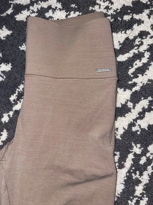 Beige leggings från Aim'n - Snygga beige leggings från Aim'n med hög midja och diskret logga framtill. Tillverkade i ett stretchigt och mjukt material som sitter skönt på kroppen. Perfekta för både träning och chill. Stilren design utan synliga sömmar på benen.