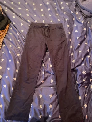 Svarta chinos med raka ben - Säljer ett par svarta chinos med raka ben och klassisk passform. Byxorna har dragsko i midjan framtill och två bakfickor med knapp. Perfekta för en clean och enkel stil. Materialet känns mjukt och lätt, troligen bomull eller bomullsblandning.