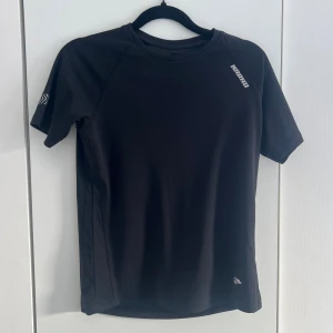 Svart tränings-tshirt  - Snygg svart tränings-tshirt från karhu med korta ärmar och rund hals. Tillverkad i ett lätt och snabbtorkande funktionsmaterial. Reflex detaljer. Perfekt för gym eller löpning.