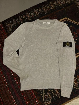 Stone Island tröja - En Stone Island tröja i grå färg till salu. Storleken är S men passar mig som är M (är 184cm lång). Tvättlappen är bortklippt. Nacken har tecken på användnibg (se bild 5) därav priset. Tröjan är äkta såklart. Skickar alltid inom 24 timmar. Skriv pm vid funderingar