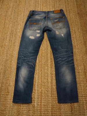 Sjuka Nudie Jeans Grim Tim - Säljer mina Nudie Jeans med sjuka fades och slitningar, modellen är Grim Tim i storleken 29:32.  Mått här 👇  Totallängd: 100 cm Midjabredd: 38 cm  Benslut: 15 cm  Skick: 	•	De är i fint skick med riktigt snygga fades och slitningar! 	 	•	Grim Tim är nudies mest populära modell!  Fråga gärna om du vill ha fler bilder! Pris ej hugget i sten!  Kolla min profil för liknande plagg! 😊