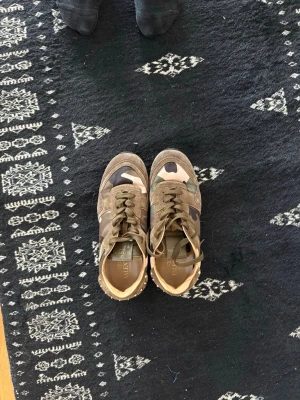Valentino camo sneakers med nitar - Snygga sneakers från Valentino med camomönster i grönt, brunt och beige. Skorna har coola nitar runt sulan och detaljer i mocka. Perfekta för dig som vill sticka ut med en unik och trendig look.