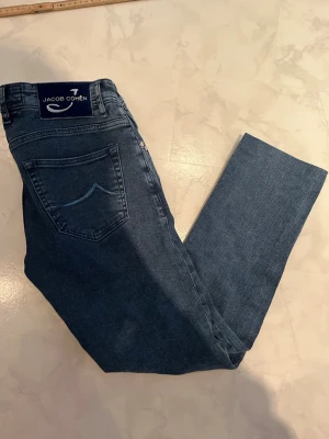 Jacob Cohen Jeans - Snygga mörkblå jeans från Jacob Cohen med klassisk femficksmodell och raka ben. Jeansen har en diskret broderad detalj på bakfickan och patch med logga i midjan. Tillverkade i mjukt denimtyg som ger en skön passform och stilren look.