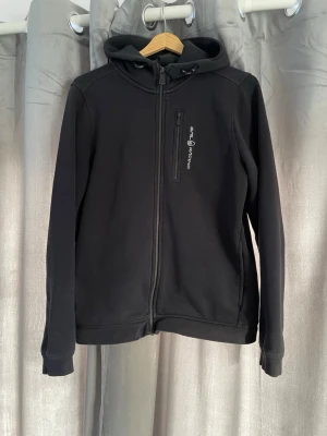Svart hoodie från Sail Racing - En fin svart zip hoodie från Sail racing, Hoodien är använd ungefär 10 gånger och har sin vanliga svarta färg. Tröjan är i storlek 176 och sitter som en S/M