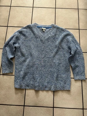 Blåmelerad stickad tröja med V-ringning storlek 44/46 - Säljer en blåmelerad stickad tröja med V-ringning och avslappnad passform. Tröjan har långa ärmar och ribbade muddar vid ärmslut och nederkant. Perfekt för dig som gillar en chill och stilren look. Materialet känns mjukt och bekvämt.