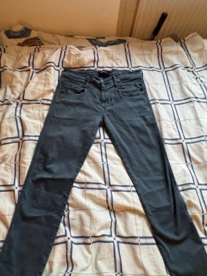 Mörkgrå Replay Hyperflex jeans - Säljer ett par mörkgrå Replay Hyperflex jeans med slim fit och klassisk femficksdesign. Jeansen har stretchigt material för extra komfort och snygg passform. Perfekta för dig som vill ha stilrena och bekväma jeans med modern look.