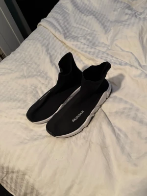 Balenciaga Speed Trainer svarta sneakers - Svarta Balenciaga Speed Trainer sneakers med vit sula och stickad ovandel i textil. Strumpliknande passform och tydlig Balenciaga-logga på sidan. Snygg och futuristisk design som sticker ut bland sneakers.
