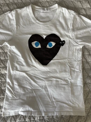 Vit t-shirt med svart hjärta från Comme des Garçons - Säljer en vit t-shirt från Comme des Garçons PLAY med ett stort svart hjärta med ögon tryckt på bröstet. Hör av er vid ytterligare frågor! Mvh