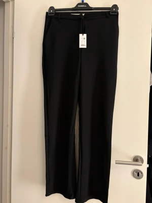 Svarta kostymbyxor låg midja oanvända  - Stilrena svarta kostymbyxor  med raka ben och klassisk midja. Byxorna har bälteshällor och diskreta fickor framtill. Perfekta för en clean och snygg look. Materialet känns mjukt och följsamt.