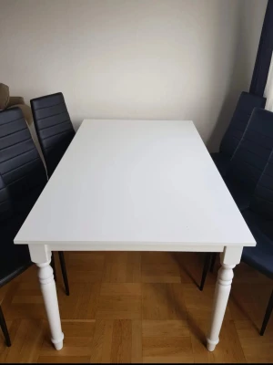 Matbord med sex svarta stolar - Säljer ett rektangulärt vitt matbord med svarvade ben och sex svarta stolar i konstläder med höga ryggstöd och metallben. Bordet har en stilren design och stolarna har horisontella sömmar för extra detalj. Perfekt för kök eller matsal.