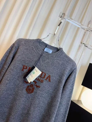 Grå stickad tröja  - Snygg grå stickad tröja  med rund halsringning och ribbade muddar. Tröjan har ett brunt broderat Milano-tryck och emblem på bröstet. Perfekt för dig som gillar exklusiva och stilrena plagg.