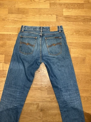 Blå jeans från Nudie Jeans - Säljer ett par klassiska blå jeans från Nudie Jeans med raka ben och snygga detaljer på bakfickorna. Är nästan som nya! Ordinarie pris 1600 kr.