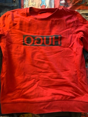 Röd sweatshirt från HUGO - Snygg röd sweatshirt från HUGO med svart logga tryckt i spegelvänd stil på bröstet. Tröjan har rund halsringning och ribbade muddar vid ärmslut och nederkant. Tillverkad i mjukt bomullsmaterial som känns skönt mot huden.