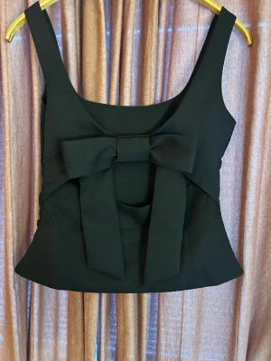 Svart linnetopp med stor rosett - Trendig svart linnetopp med breda axelband och en stor dekorativ rosett baktill. Toppen har en figurnära passform och är perfekt för att skapa en lyxig känsla 🥰