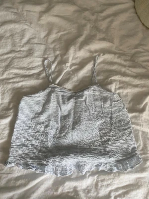 Ljusblå rutig linnetopp med volang - Säljer ett ljusblått pyjamaslinne med tunna axelband, vit mini spets och volangkant nedtill. I storlek 158/164 men sitter som XS.