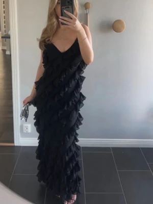 Svart långklänning med volanger - Säljer en svart långklänning med tunna axelband och v-ringning. Bara använt klänningen ett tillfälle.