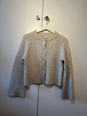 Beige kofta  - Mysig beige kofta i mjukt stickat material med rund halsringning och ribbade muddar. Croppad modell med fem knappar framtill. Perfekt att slänga över en t-shirt eller linne för en fin look😉! 