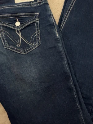 Mörkblå jeans från Gina Tricot - Snygga mörkblå jeans från Gina Tricot med dekorativa vita sömmar och unik fickdetalj bak. Klassisk femficksmodell i stretchigt denimtyg som sitter skönt. Perfekta för dig som gillar en enkel men ändå trendig look.