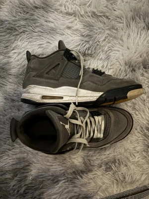 Gråa Air Jordan 4 Retro sneakers - Snygga Air Jordan 4 Retro sneakers i grå mocka med svarta och vita detaljer. Fortfarande bra skick och är mest smutsiga. Liten skada inne vid baksidan / hälen. Självklart öppen för prisförslag och köper du fler varor av mig får du mängd rabatt.
