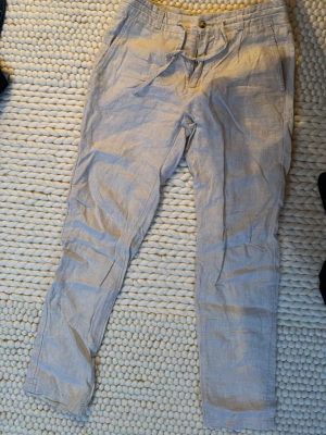 Beige linnebyxor med knytband från bondelid - Snygga beige linnebyxor med avslappnad passform och knytband i midjan. Byxorna har fickor fram och en bakficka med knapp. Perfekta för en varm dag.