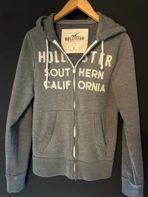 Hollister Grå zip-hoodie  - En perfekt Grå zip-hoodie från Hollister inför våren. Stor vit text på bröstet med 'Hollister Southern California'. Väldig eftertraktad hoodie utan skador & deflekter😁💯