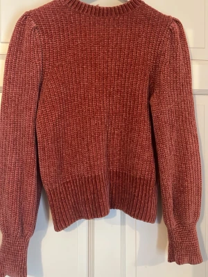 Roströd stickad tröja med puffärm - Mysig roströd stickad tröja med bred ribbstickning och puffiga ärmar. Tröjan har rund halsringning och extra breda muddar vid ärmslut och nederkant. Perfekt för lager på lager och ger en trendig siluett.