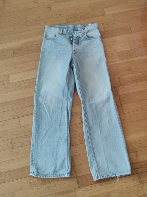 Hope Criss - Säljer ett par ljusblå jeans med rak/vid passform. Jeansen har knäppning framtill, klassiska fem fickor och råa, avklippta benslut för en trendig look. Perfekta för dig som gillar en avslappnad och cool stil. W28 L32