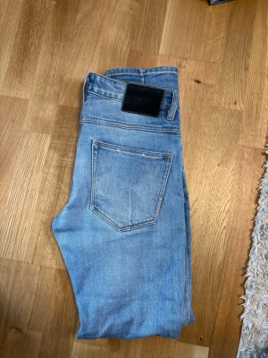 Neuw jeans slim - Säljer ett par ljusblå jeans med rak passform och klassisk femficksdesign. Jeansen har en svart patch bak i midjan och är tillverkade i denim. Perfekta för en avslappnad och trendig look.