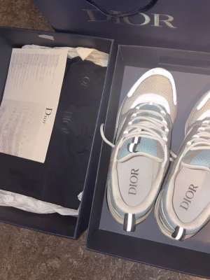  sneakers i beige och blå - Säljer ett par  sneakers i beige, vitt och blått med mesh och läderdetaljer. Skorna har chunky sula, reflekterande inslag och klassisk logga på plösen. Snygg och modern design som sticker ut. Levereras i originalkartong med dustbag.