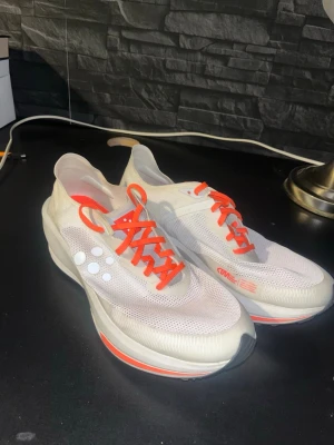 Vita Saucony Endorphin Pro sneakers - Säljer ett par vita Saucony Endorphin Pro sneakers med mesh-ovandel och röda detaljer. Skorna har röda snören, vita prickar på sidan och tjock sula med röda inslag. Perfekta för dig som gillar sportig och modern stil. Ny pris 2000