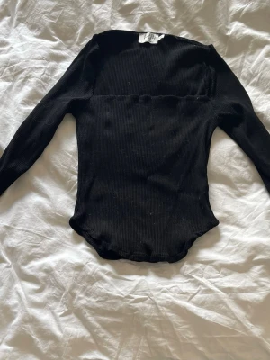 Svart ribbad långärmad topp från NA-KD i storlek M - En svart, ribbad långärmad topp från NA-KD i storlek M i fint skick.Tight passform och stretchigt material som ger en snygg siluett. Perfekt att styla med jeans eller kjol för en trendig look.