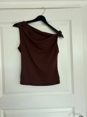 Brun oneshoulder topp - Trendig, snygg brun topp med oneshoulder-design. Storlek M. Köptes second hand men etiketten är bortklippt så oklart märke🤗