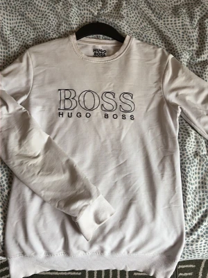 Vit sweatshirt från Hugo Boss - Snygg vit sweatshirt från Hugo Boss med broderad logga på bröstet. Tröjan har rund halsringning, långa ärmar och ribbade muddar. Perfekt för en clean och stilren look.