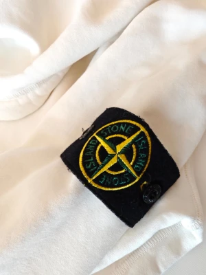 Vit hoodie från Stone Island. Mycket fint skick - Säljer en clean vit hoodie från Stone Island med klassisk patch på ärmen. Hoodien har huva med dragsko och en stor magficka framtill. Tillverkad i mjukt bomullsmaterial som känns riktigt skönt mot huden. Perfekt för dig som gillar streetwear och vill ha något stilrent. Förutom lite på insidan av huvan så är den perfekt.  100 % äkta