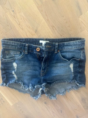 Blå jeansshorts  - Snygga blå jeansshorts från H&M med fransig kant och slitna detaljer framtill i storlek 36, passar även 34. Brukar dra ner för att de ska bli mer lågmidjade, knappt använda💕