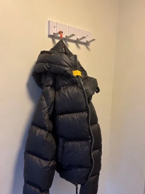 Svart dunjacka från Parajumpers - Säljer en svart dunjacka från Parajumpers med klassisk PJS-logga på ärmen och gul detalj vid halsen. Jackan har hög krage, dragkedja och snöre för justering. Perfekt för kalla vinterdagar och riktigt varm.