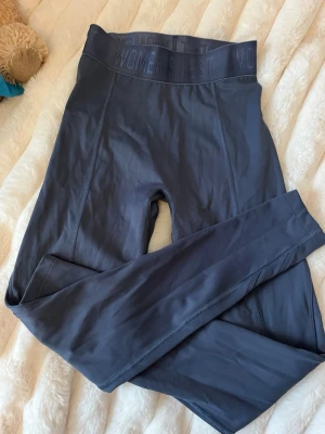 Mörkgrå tights från Women's Best - Snygga mörkgrå träningstights från Women's Best med hög midja och bred resår med logga. Tillverkade i ett stretchigt och mjukt material som passar perfekt för gym eller löpning. Snygg passform och diskreta sömmar för en stilren look.