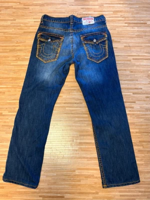 True religion super T jeans w31 - Saljer ett par riktig feta True Religion jeans i storlek W31. Klassiska modellen "logan" med ikoniska bakfickor, kraftiga gula sömmar och snygg distressed/faded wash. Bra skick med distressing, dock "lagade" under distressen av tidigare ägare (se sista bild), märks däremot inte alls vid användning. Rak/relaxed fit beroende på kroppstyp. True to size. Öppen för prisförslag!