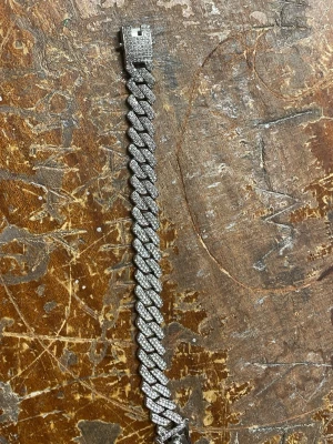 Silverfärgat cuban länkarmband - Stilrent armband i cuban länkdesign med silverfärg och gnistrande stenar på ovansidan. Låset är dekorerat med små stenar för extra bling. Perfekt accessoar för dig som gillar att sticka ut med detaljer. Materialet ser ut att vara metall med stenar.