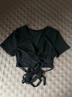 Svart omlottopp med knyt från SHEIN - Trendig svart omlottopp från SHEIN med korta ärmar och djup v-ringning. Toppen har långa knytband i midjan som kan snurras runt och knytas för en snygg look. Perfekt att styla med jeans eller kjol.